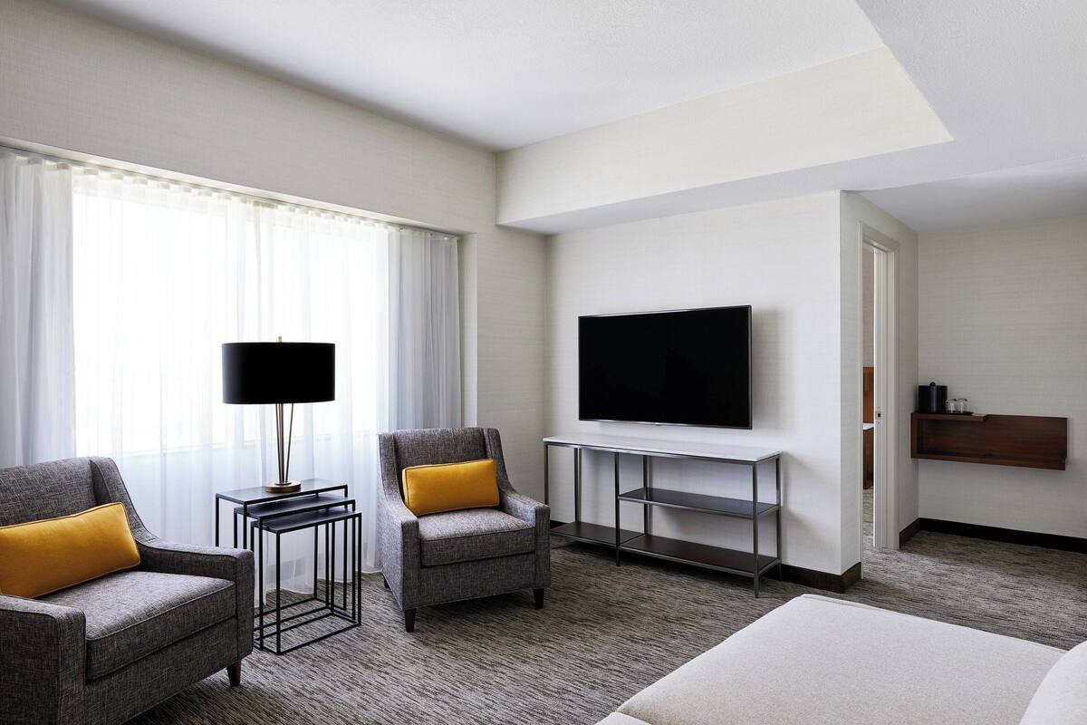 A hotel room with two armchairs, a TV, a desk, and a bed.
