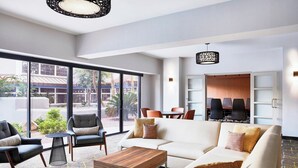 A modern hotel lobby with a white sofa, armchairs, a coffee table, and a dining area with chairs and a table. Large windows provide a view of the outdoors. - Delta Hotels by Marriott Phoenix Mesa (Mesa)