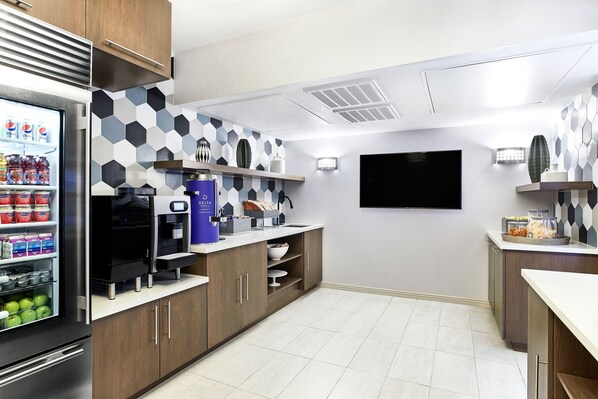 Una cocina moderna con refrigerador, cafetera y televisor de pantalla plana montado en la pared.