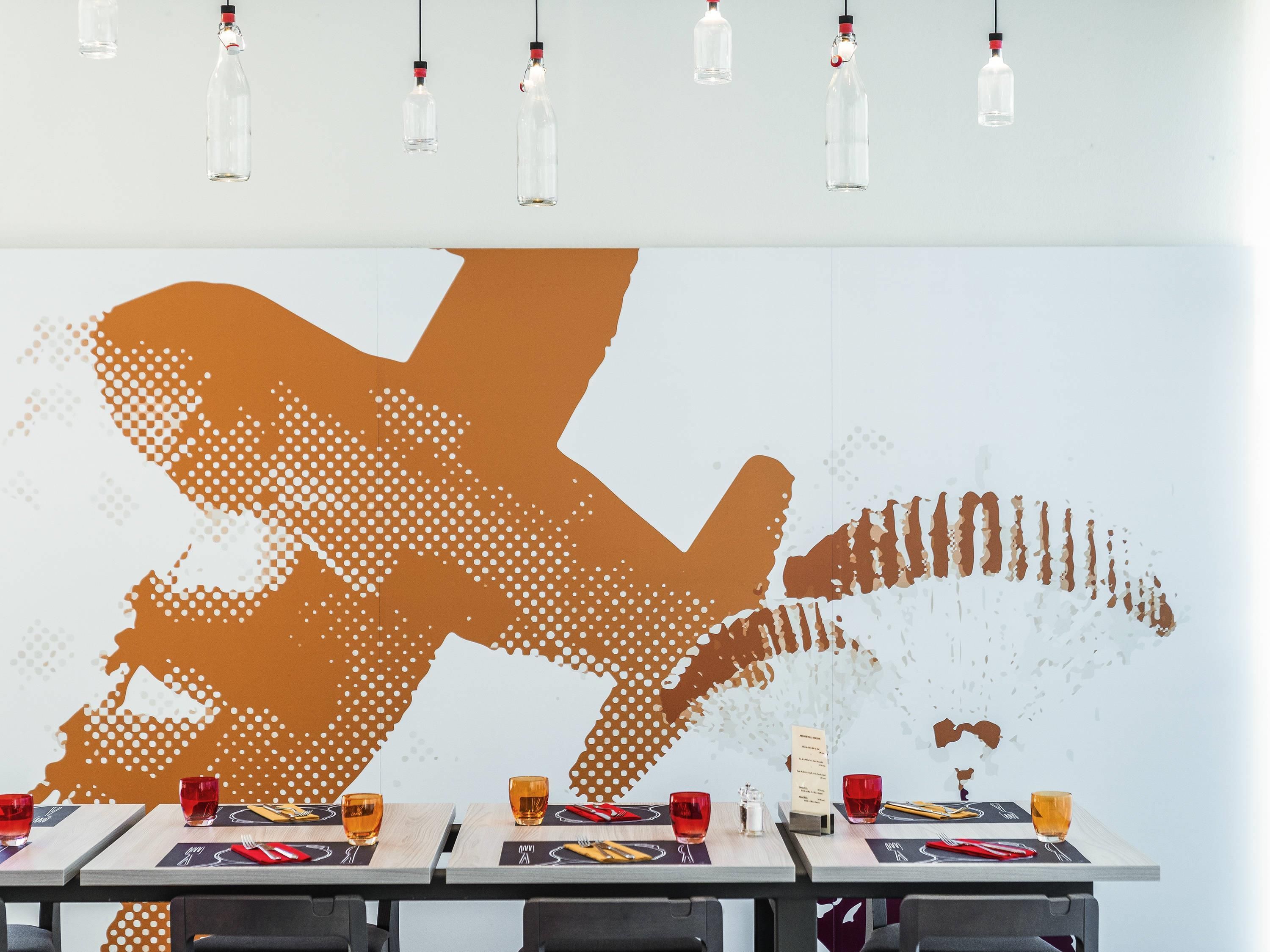 A restaurant with tables set for dining, a large wall mural, and hanging light fixtures.