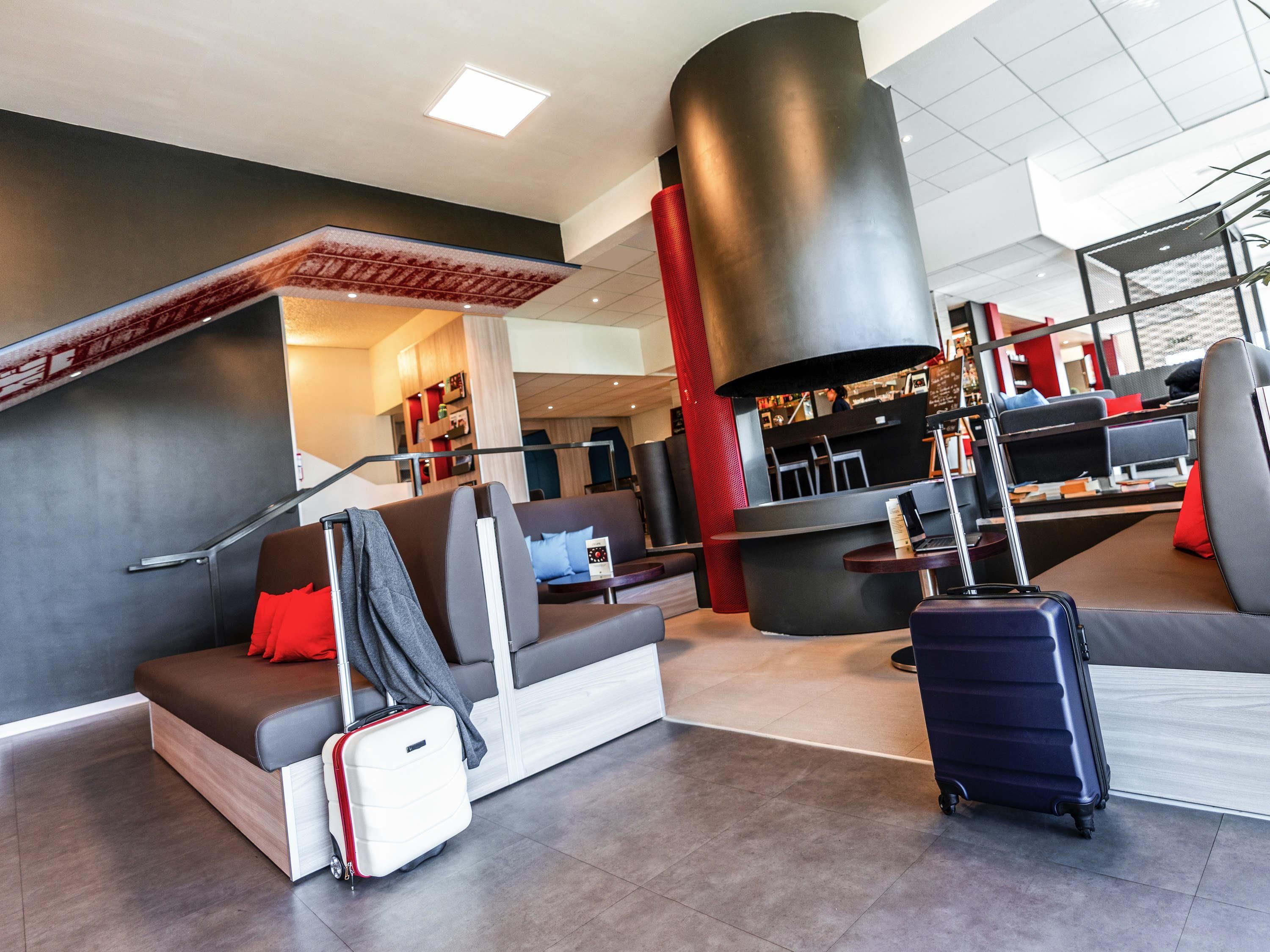 A modern lounge area with seating, a staircase, a large cylindrical structure, and luggage.