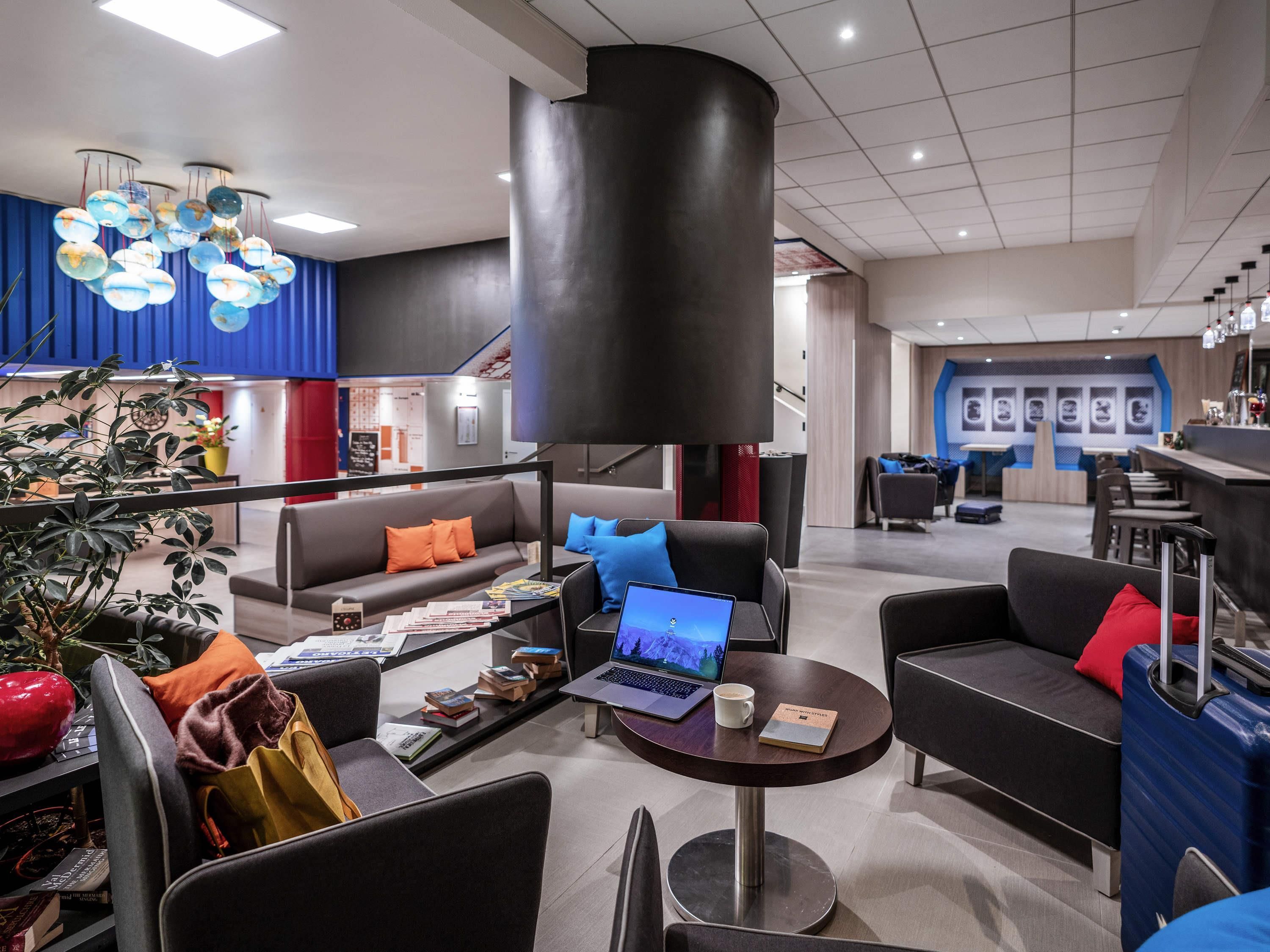A modern lobby with seating areas, a coffee table with a laptop, and a large black pillar.