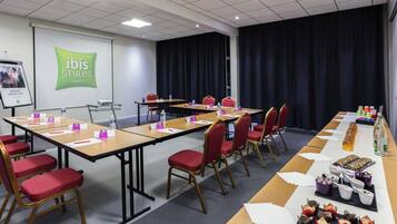 A conference room with tables, chairs, a projector screen, and a buffet table with snacks.