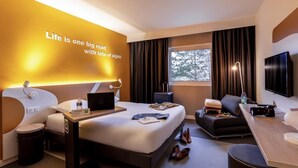 Une chambre d’hôtel moderne, dotée d’un grand lit, d’un bureau, d’une télévision et d’un mur orné d’inscriptions inspirantes.