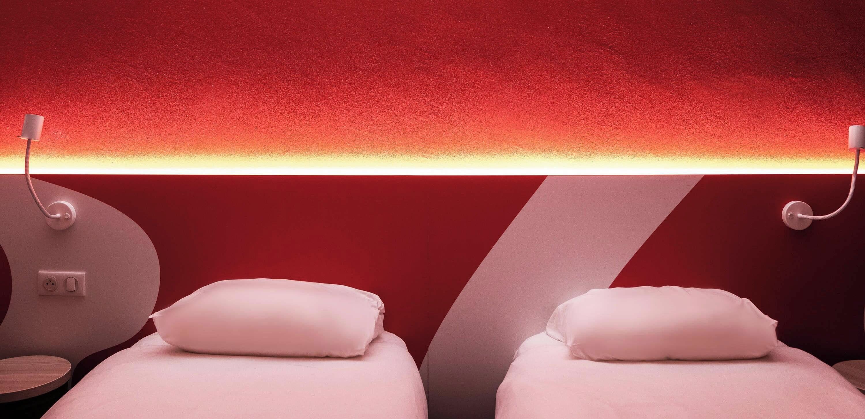 Ein Zimmer mit zwei Betten, jeweils mit Kissen und einer Wandleuchte.