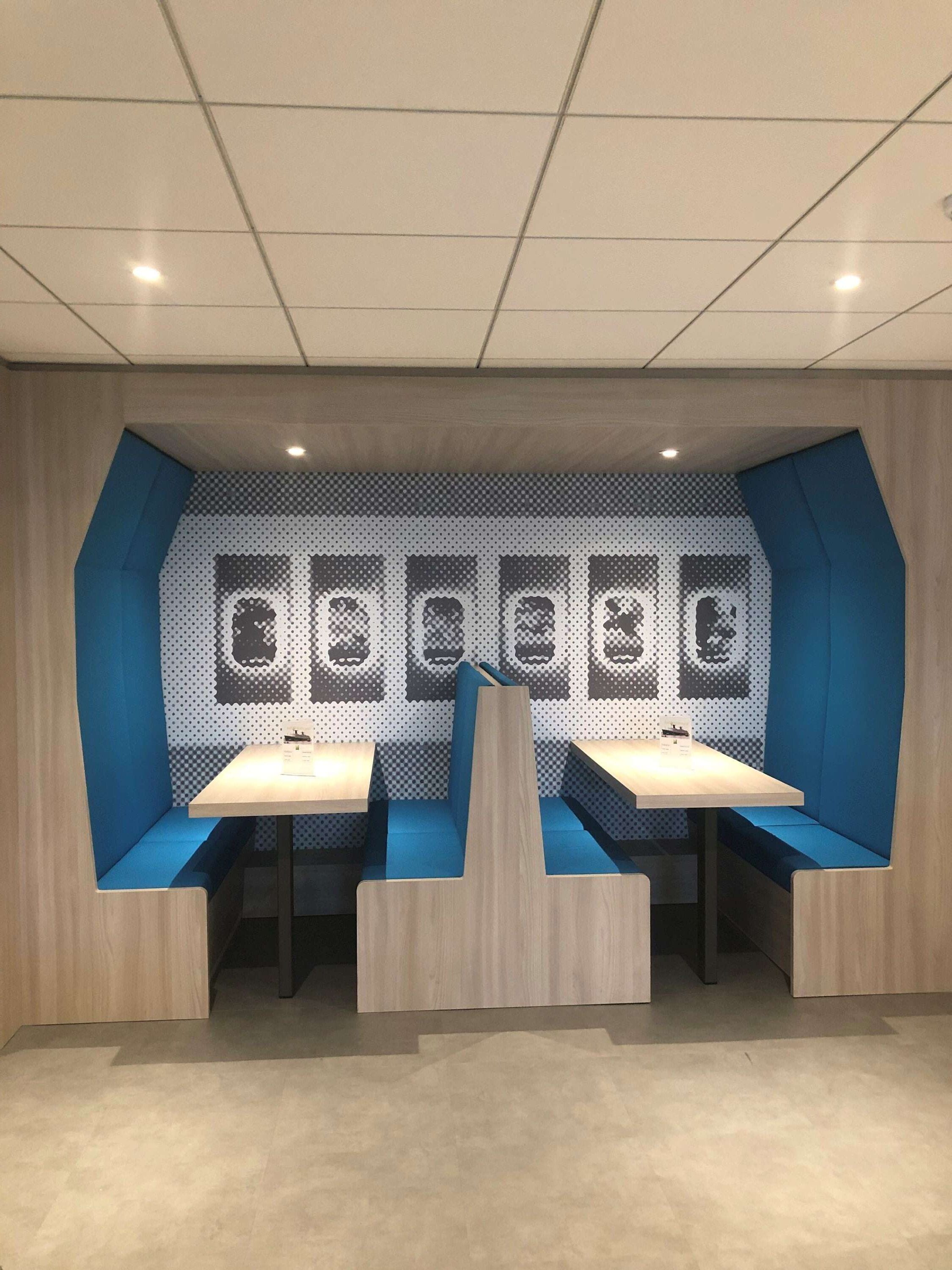 Un área de descanso moderna con bancos acolchados en azul y mesas de madera, destacando un diseño artístico único de estilo pixelado.