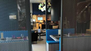 A modern dining area with a wooden table, red chairs, and a blue booth. There is a kitchen area in the background with a TV and a counter.