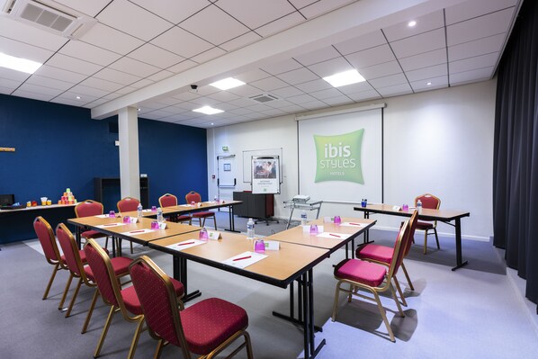 A conference room with a large screen displaying 'ibis styles hotels', multiple tables with name cards, and red chairs.