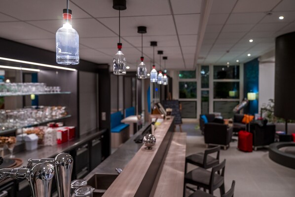 A modern bar area with hanging light fixtures, a long counter, and seating arrangements.