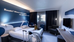 A modern hotel room with a large bed, a desk, a chair, a TV, and a window with curtains.