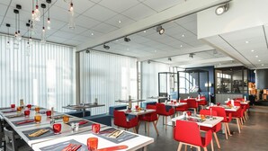 A modern restaurant with long tables, red chairs, and hanging light fixtures. - ibis Styles Beauvais (Beauvais)