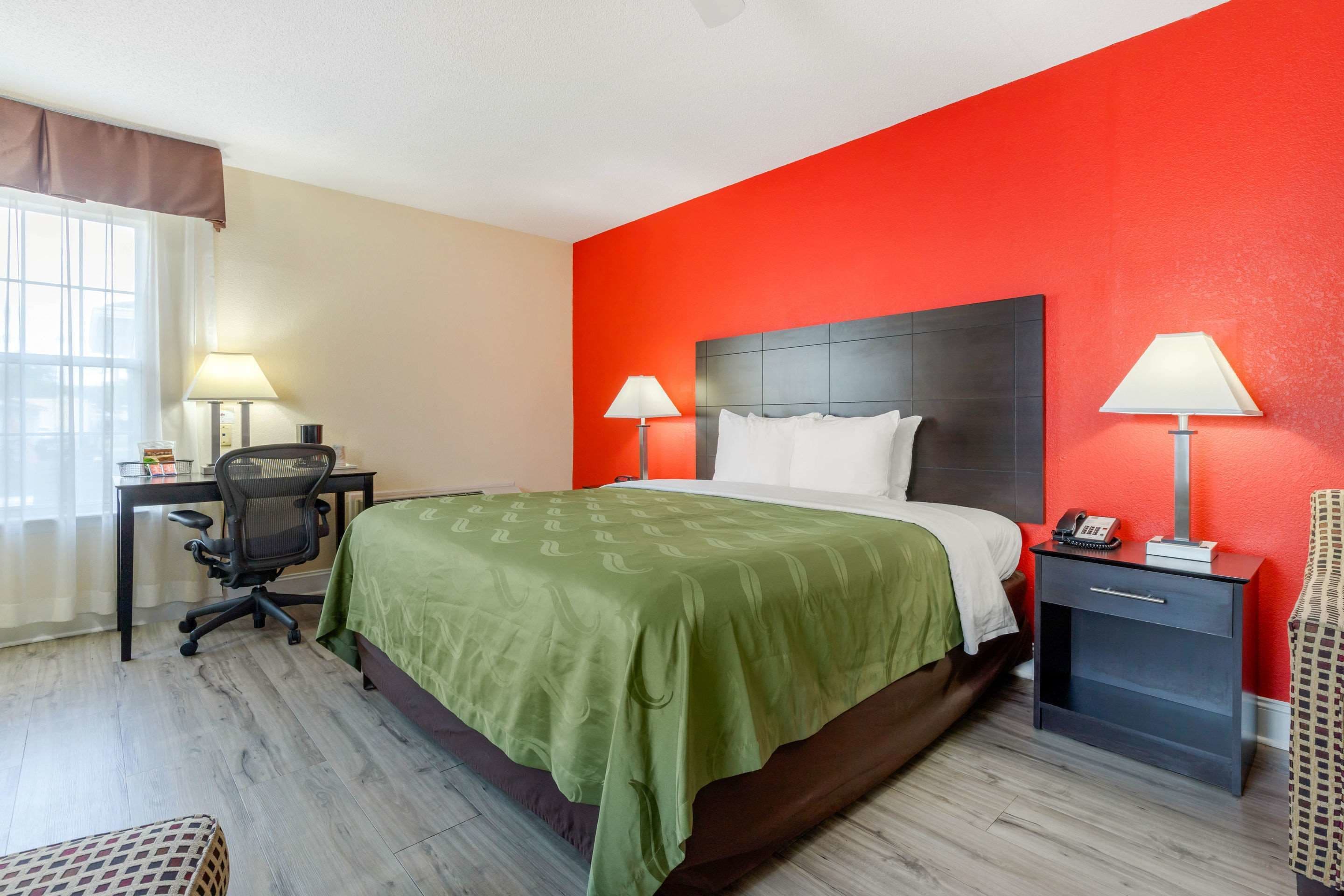 Une chambre d’hôtel avec un grand lit, deux tables de chevet avec des lampes, un bureau avec une chaise et une fenêtre avec des rideaux.