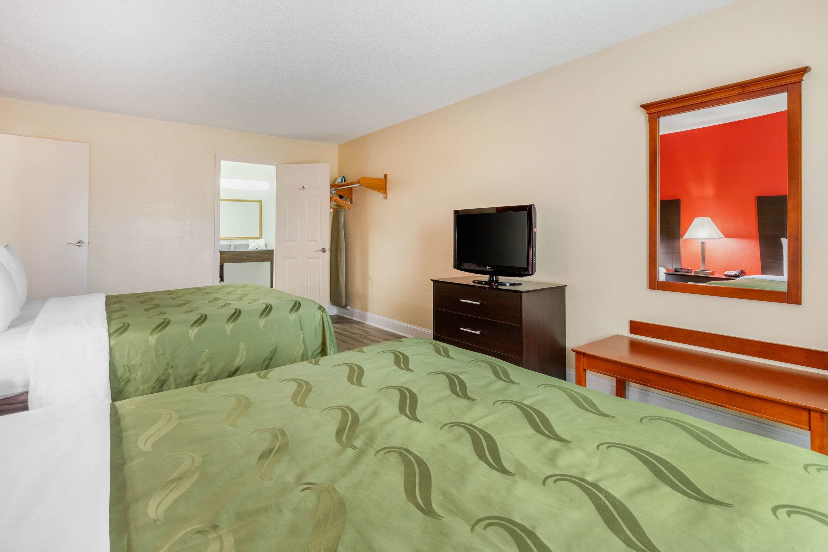 A hotel room with two beds, a television, a mirror, and a desk.