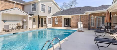 A swimming pool with a covered area, lounge chairs, and a brick building with multiple windows.