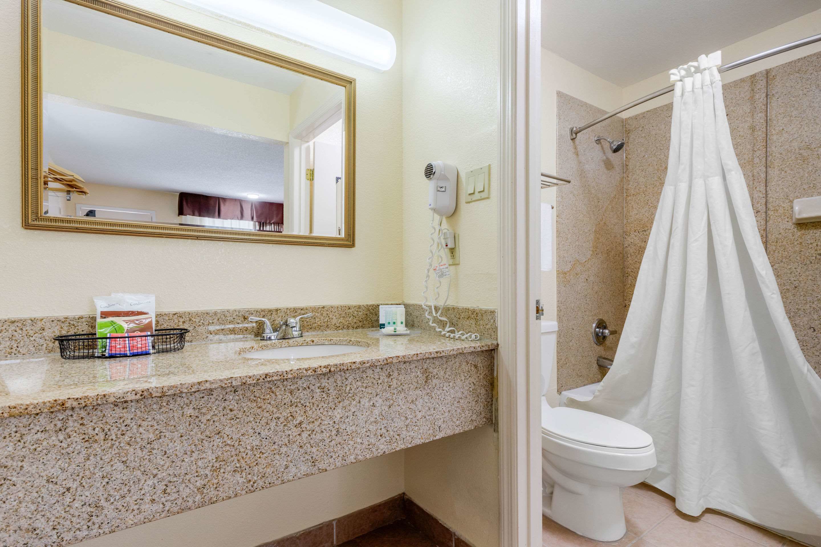 A bathroom with a granite countertop, a white sink, a mirror, a hairdryer, and a shower curtain.
