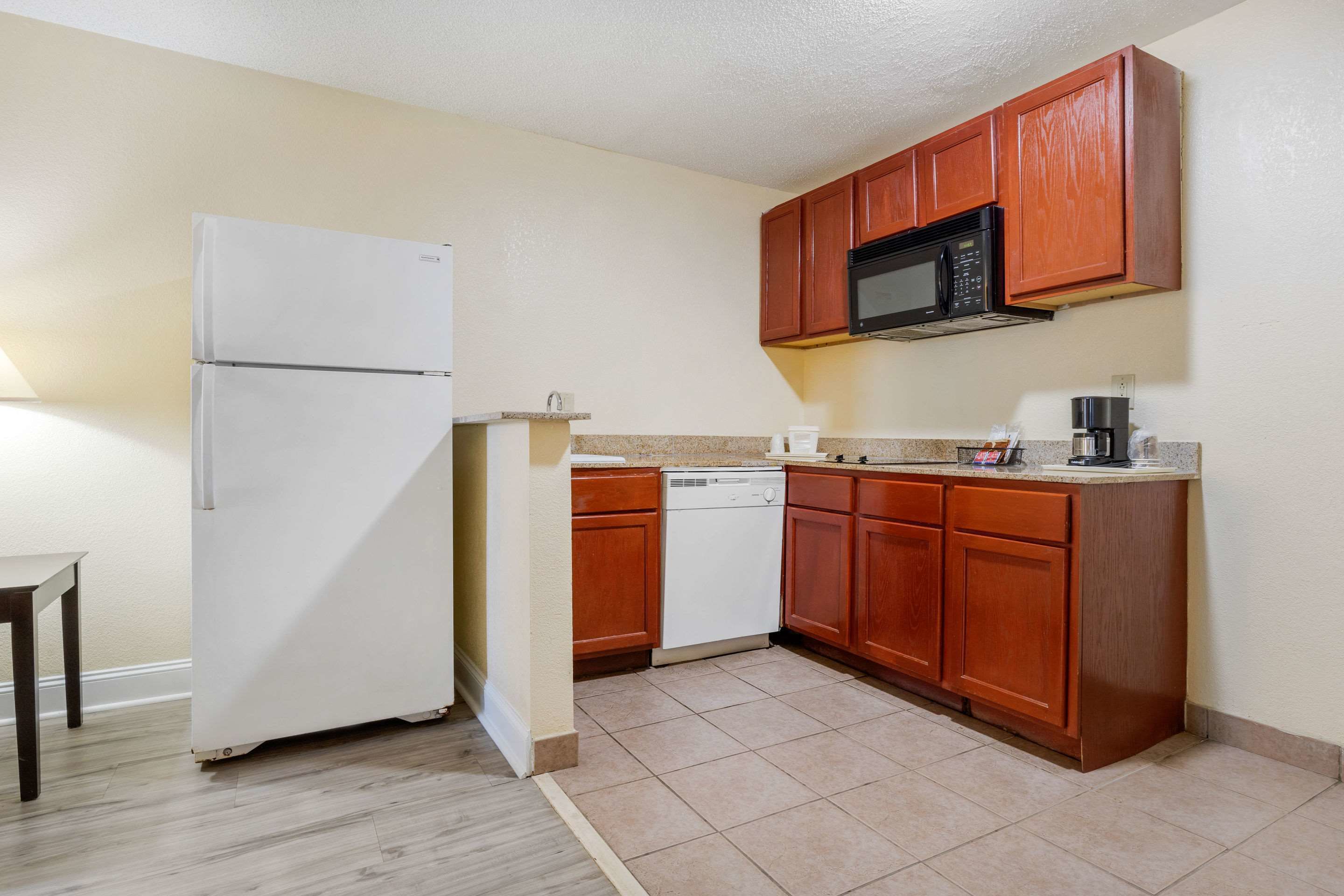 A compact kitchen with wooden cabinets, a white refrigerator, a dishwasher, and a microwave.