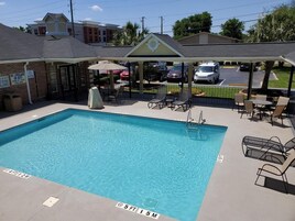 Una piscina rectangular con agua cristalina, rodeada de sillas de descanso y sombrillas.