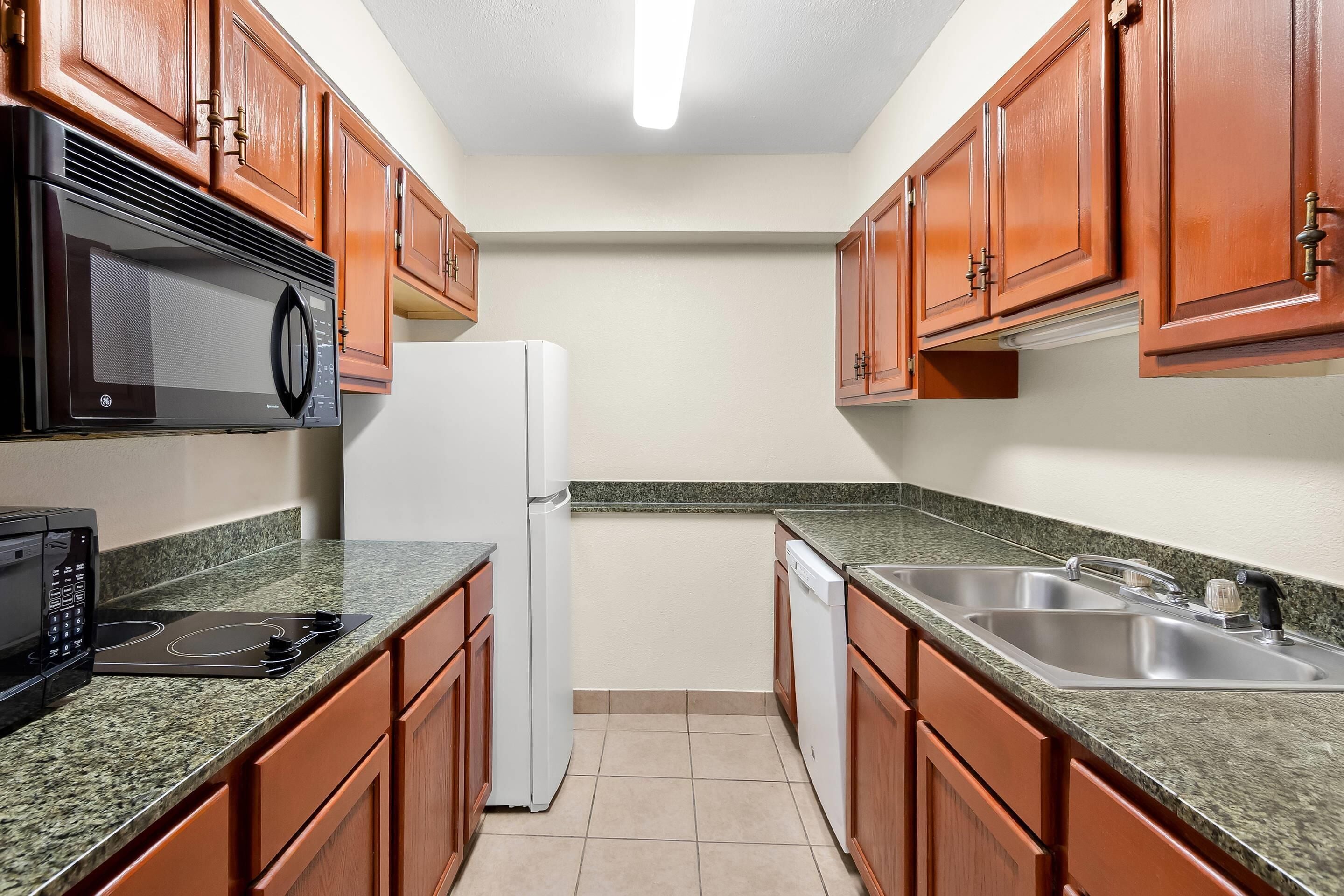 A kitchen with wooden cabinets, a microwave, a refrigerator, a dishwasher, and granite countertops.