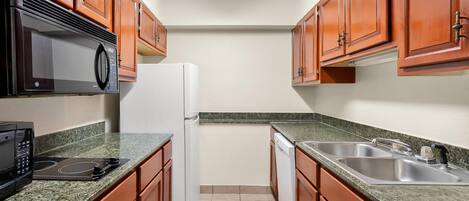 A kitchen with wooden cabinets, a microwave, a refrigerator, a dishwasher, and granite countertops.