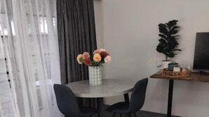 Una habitación de hotel con cama, una mesa redonda con sillas, un florero con flores, una planta en maceta y un televisor.