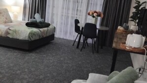 Habitación de hotel con cama, una mesita con un florero, una silla y una cafetera.