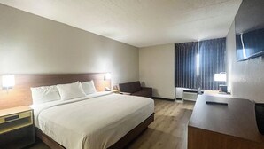 A hotel room with a bed, a desk, a chair, a TV, and a window with curtains.