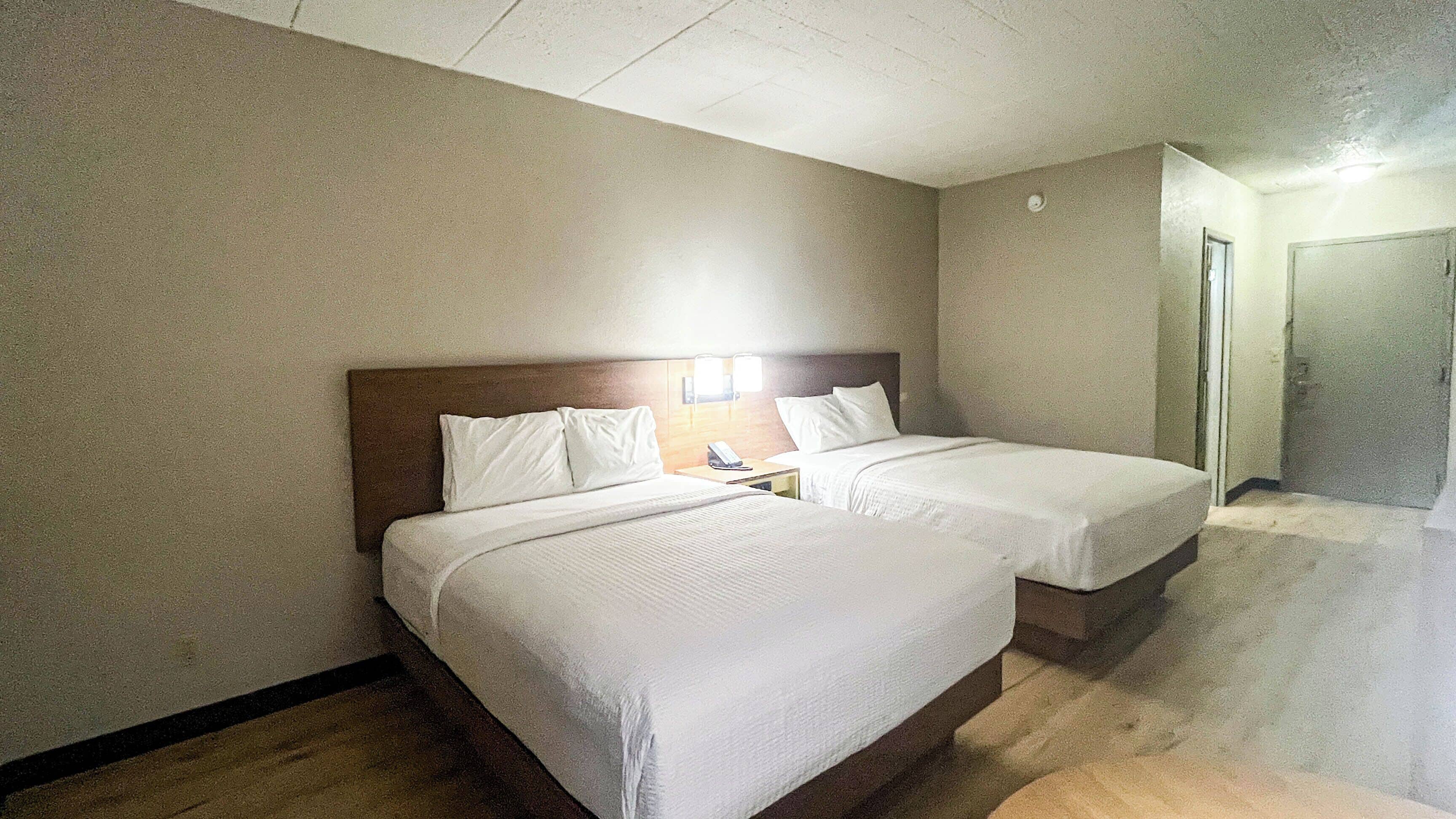 A hotel room with two beds, a wooden headboard, a bedside table with a phone, and a light fixture.