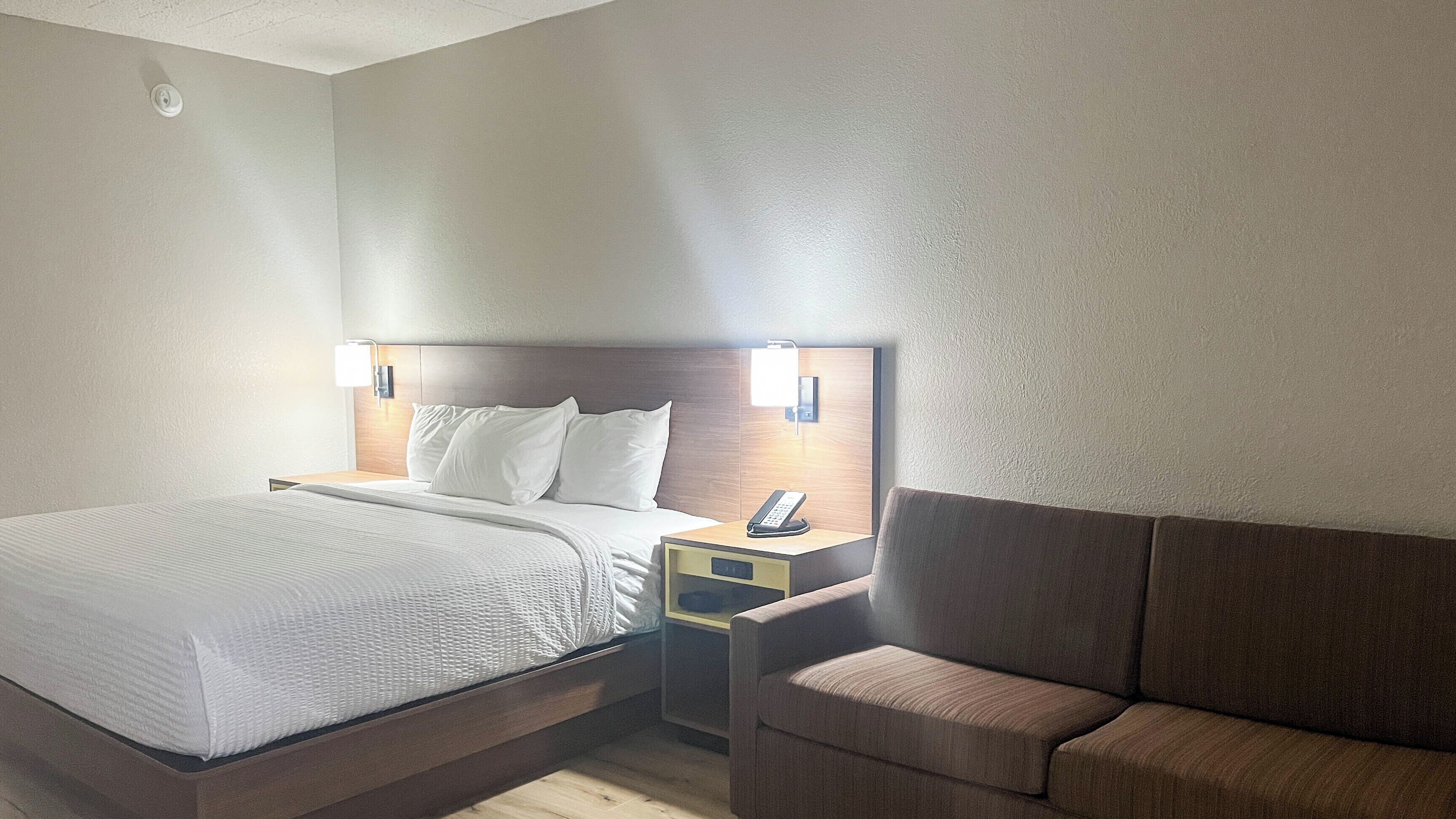 A hotel room with a bed, bedside table with a phone, a nightstand, and a sofa.