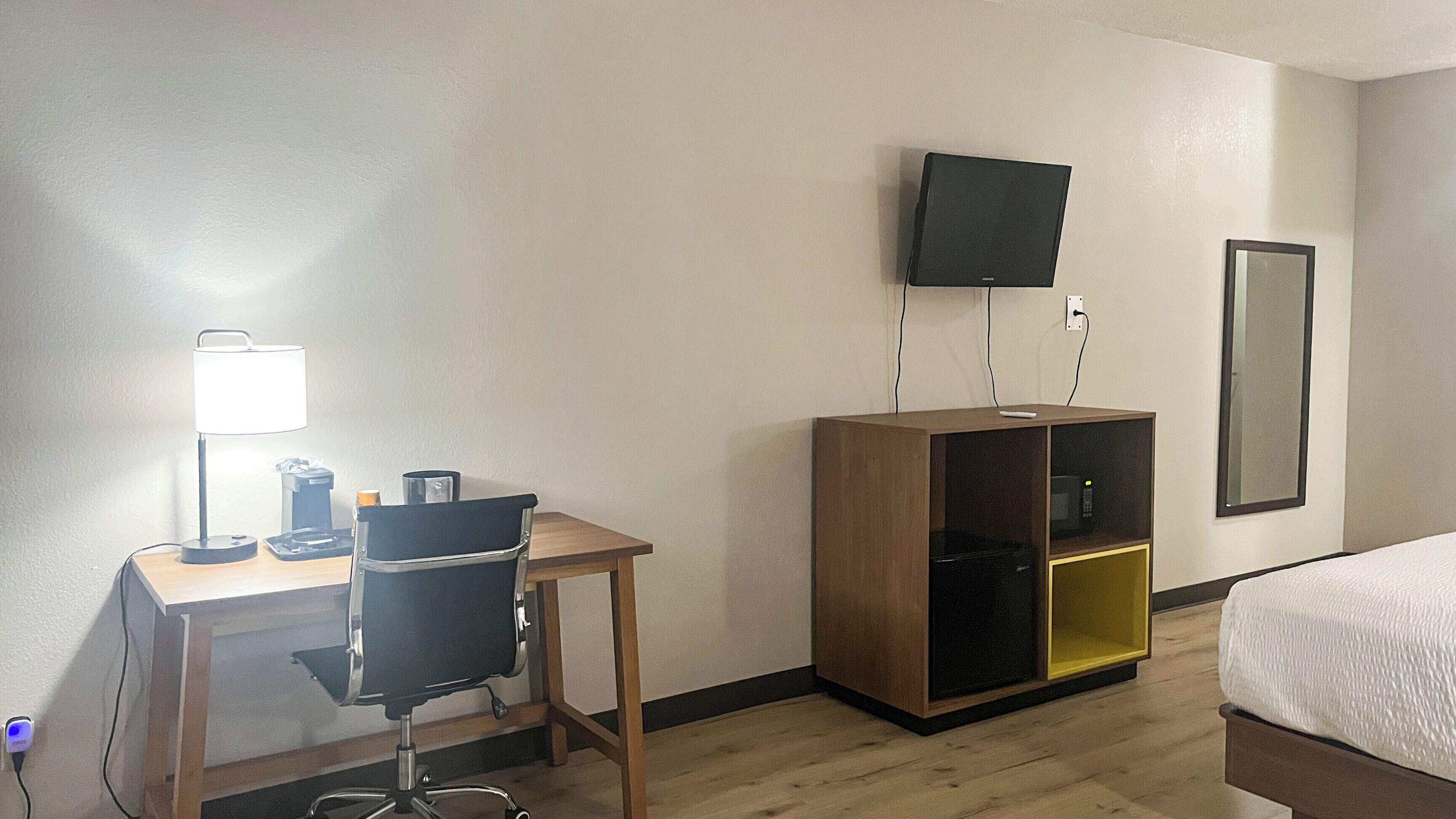 A hotel room with a desk, chair, bed, TV, and a mirror.