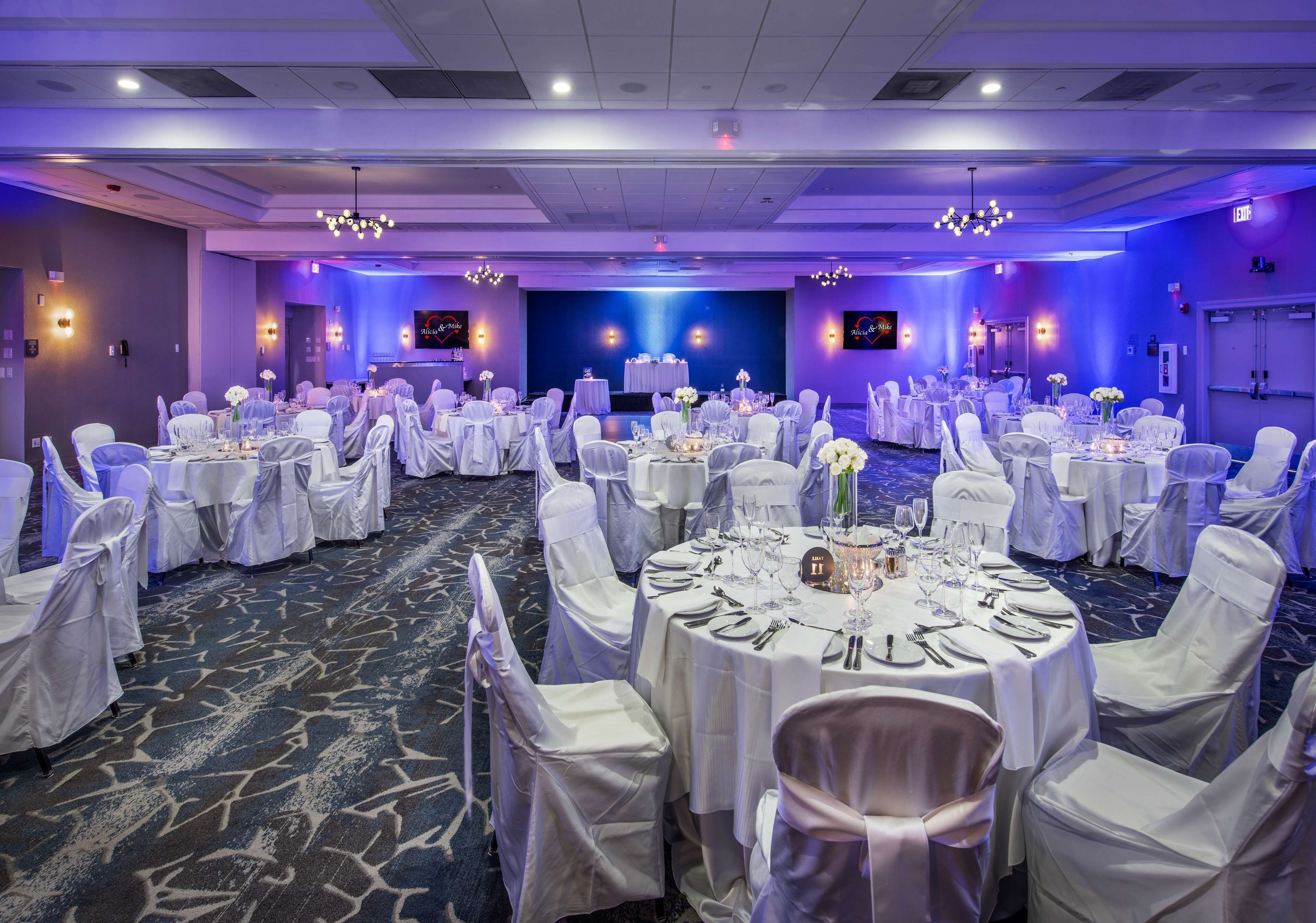 A banquet hall with round tables set for dining, white chairs, and a stage in the background.