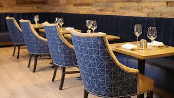Una fila de sillas tapizadas en azul con diseños geométricos, mesas de madera y un banco acolchado en azul oscuro.