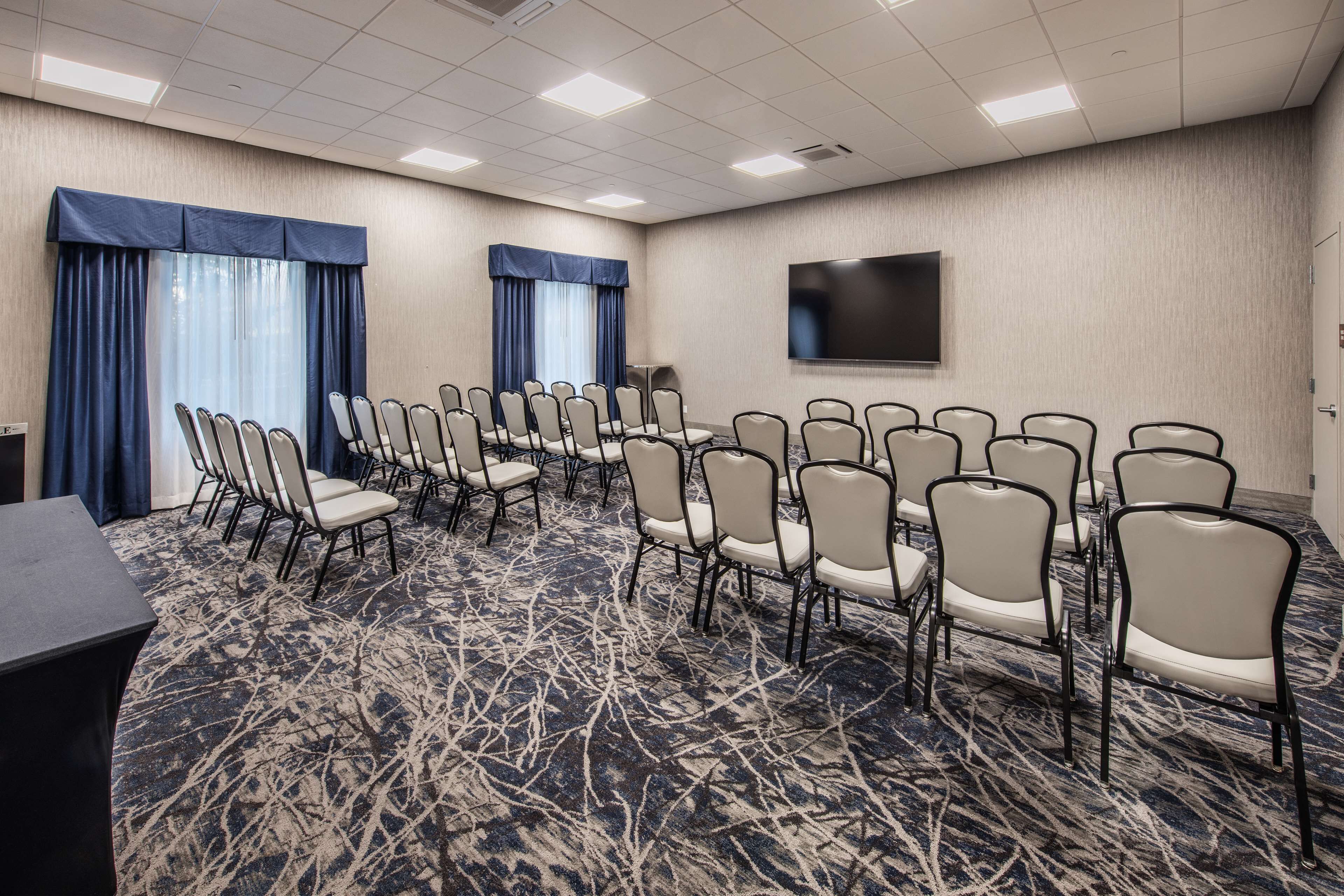 A conference room with rows of chairs, a large screen, and a carpeted floor.