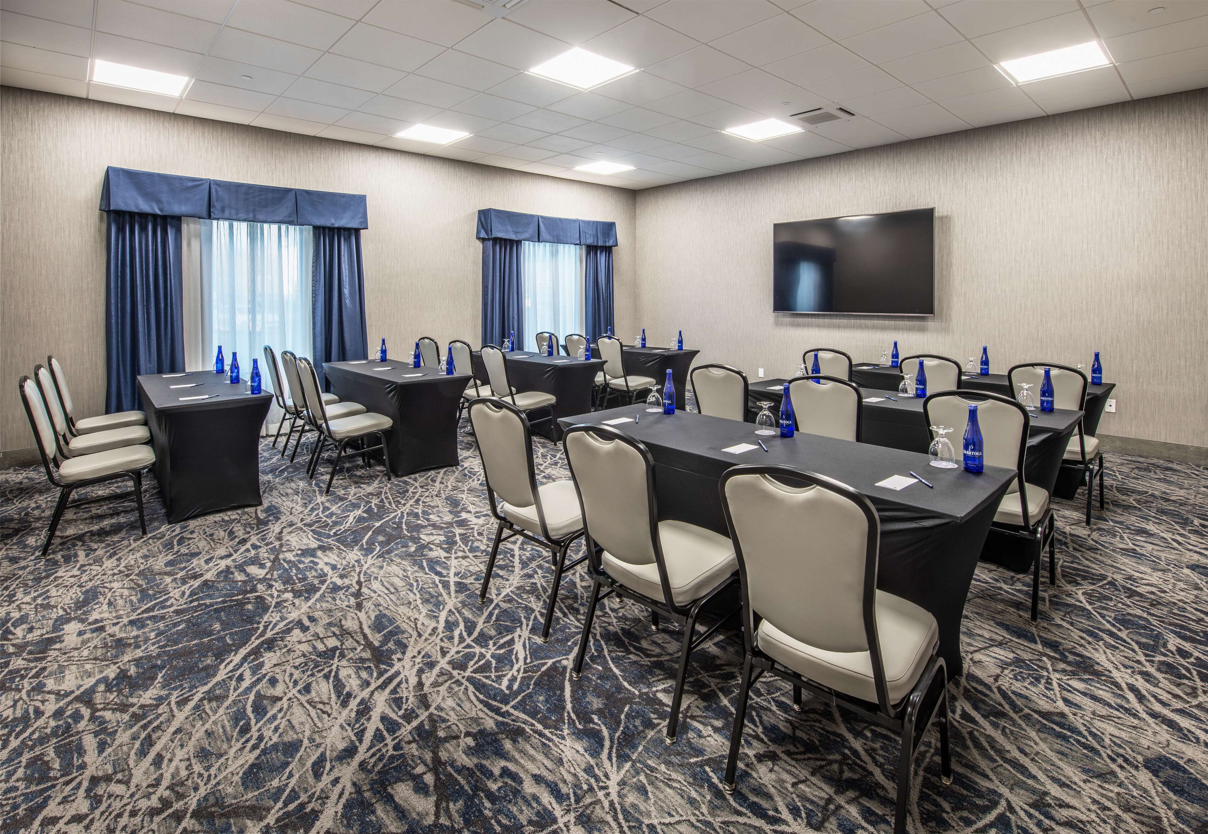 A conference room with multiple tables and chairs, a flat-screen TV, and a patterned carpet.