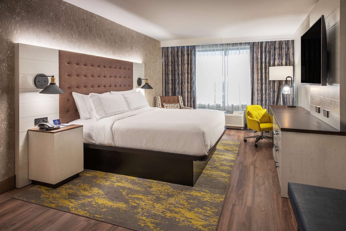 Ein modernes Hotelzimmer mit einem großen Bett, einem Schreibtisch, einem Sessel und einem Fernseher.