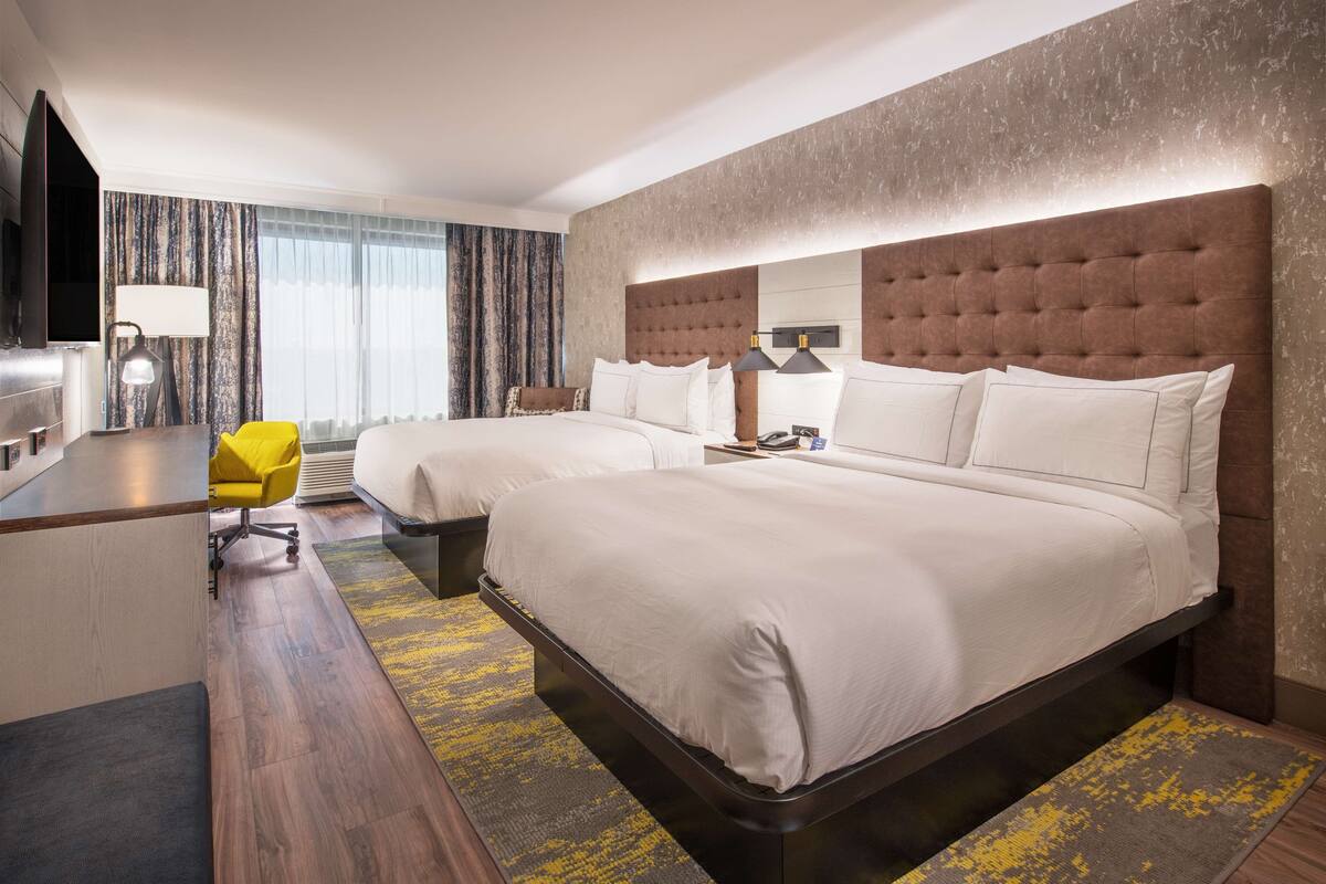 Ein Hotelzimmer mit zwei Betten, einem Schreibtisch, einem Sessel und einem Fernseher.