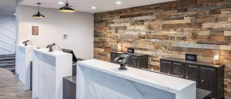 A hotel reception area with marble counters, a wooden wall, and pendant lighting.