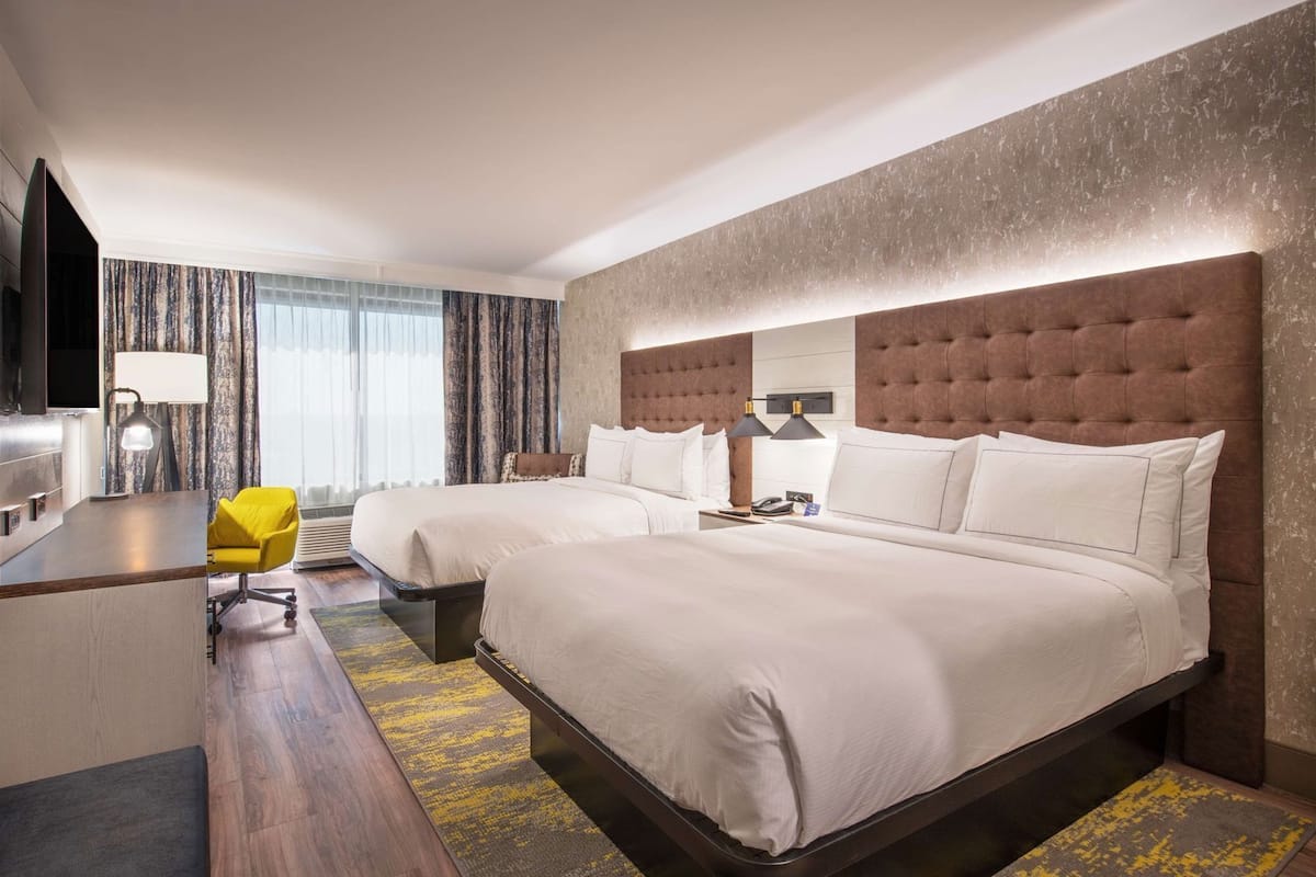Ein Hotelzimmer mit zwei Betten, einem Schreibtisch, einem Stuhl und einem Fernseher.