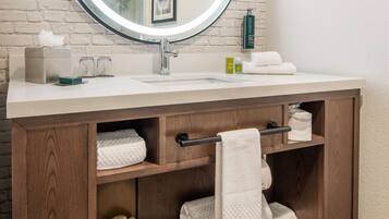 A bathroom with a round mirror, white sink, wooden vanity, and a towel rack.