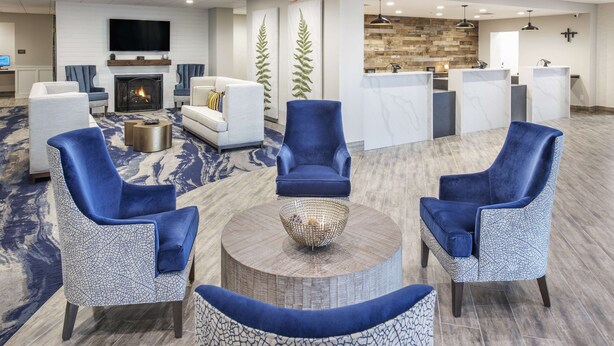 A modern hotel lobby with a fireplace, seating area, reception desk, and a stone wall. - Doubletree by Hilton Monroe Township Cranbury (Monroe Township)
