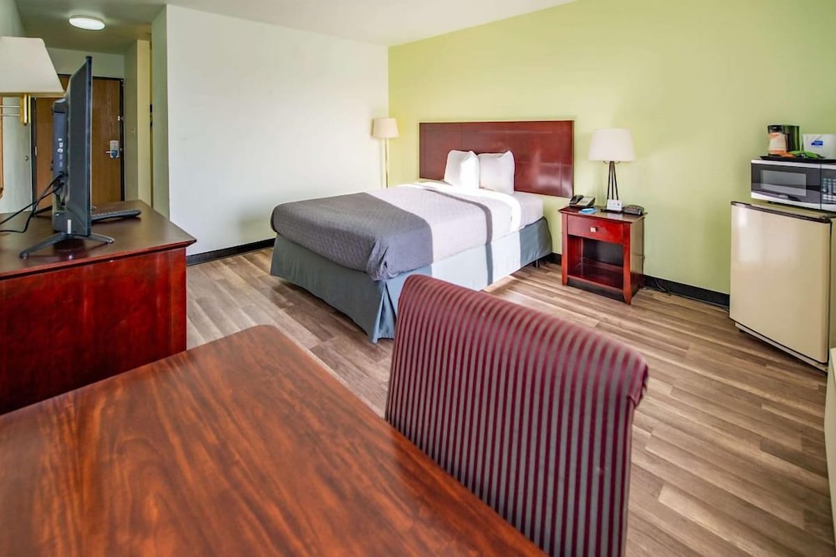 A hotel room with a bed, desk, chair, and a microwave.