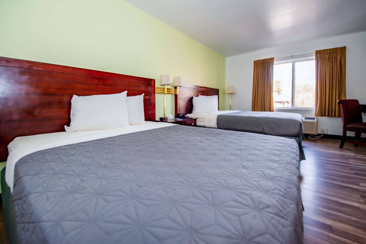 A hotel room with two beds, a desk, a chair, and a window with curtains.