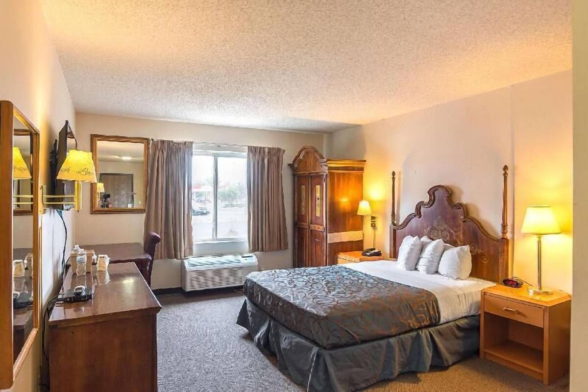 A hotel room with a bed, bedside lamps, a desk with a chair, a wardrobe, and a window with curtains.