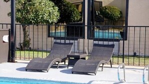 A pool area with lounge chairs and a fence.