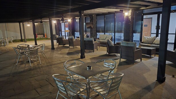 An outdoor patio area with metal tables and chairs, wicker sofas, and a stone fireplace.