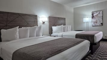 A hotel room with two beds, a headboard with a geometric design, a wall-mounted lamp, and a framed artwork.
