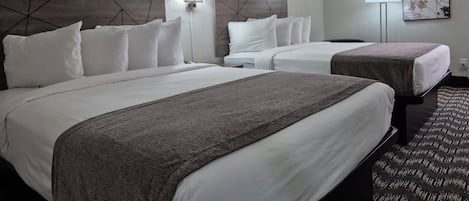 A hotel room with two beds, a headboard with a geometric design, a wall-mounted lamp, and a framed artwork.