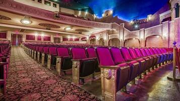 Een theater met rijen rode stoelen, een versierd plafond en een gekleurd tapijt.
