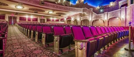 A theater with rows of red seats, ornate ceiling, and patterned carpet.
