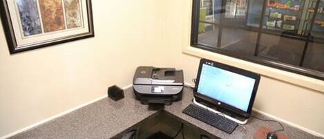 A small office with a printer, a laptop, and a framed picture on the wall.
