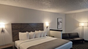 A hotel room with a large bed, bedside lamps, a desk, a chair, and a wall-mounted artwork.